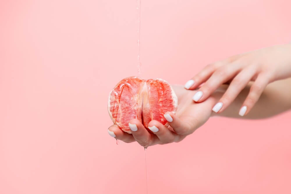 Woman's Elegant Hands Hold Half A Grapefruit. Oil Is Poured On Top Of The Fruit. The Concept Of Sexuality.