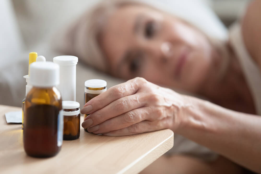 Close Up Focus On Wrinkled Female Hand Taking Glass Bottle With Pills