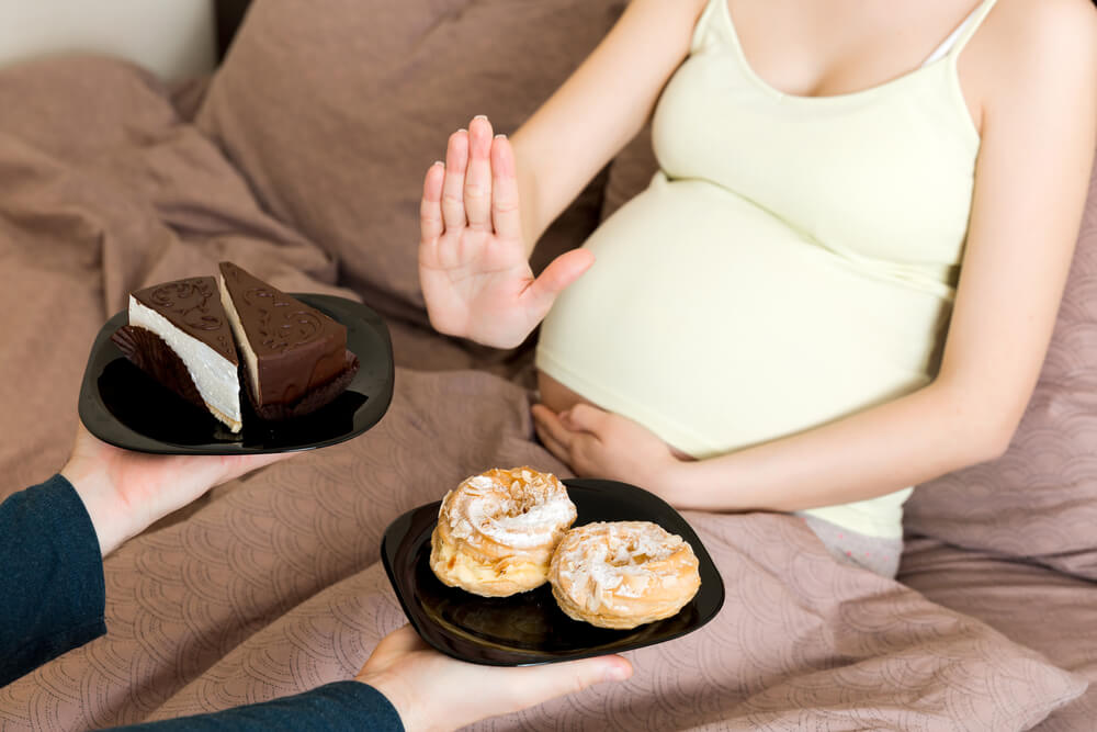 Close Up Of Pregnant Woman Relaxing In Bed Refuses Delicious Slices Of Cakes And Makes Stop Gesture Diet During Pregnancy Concept