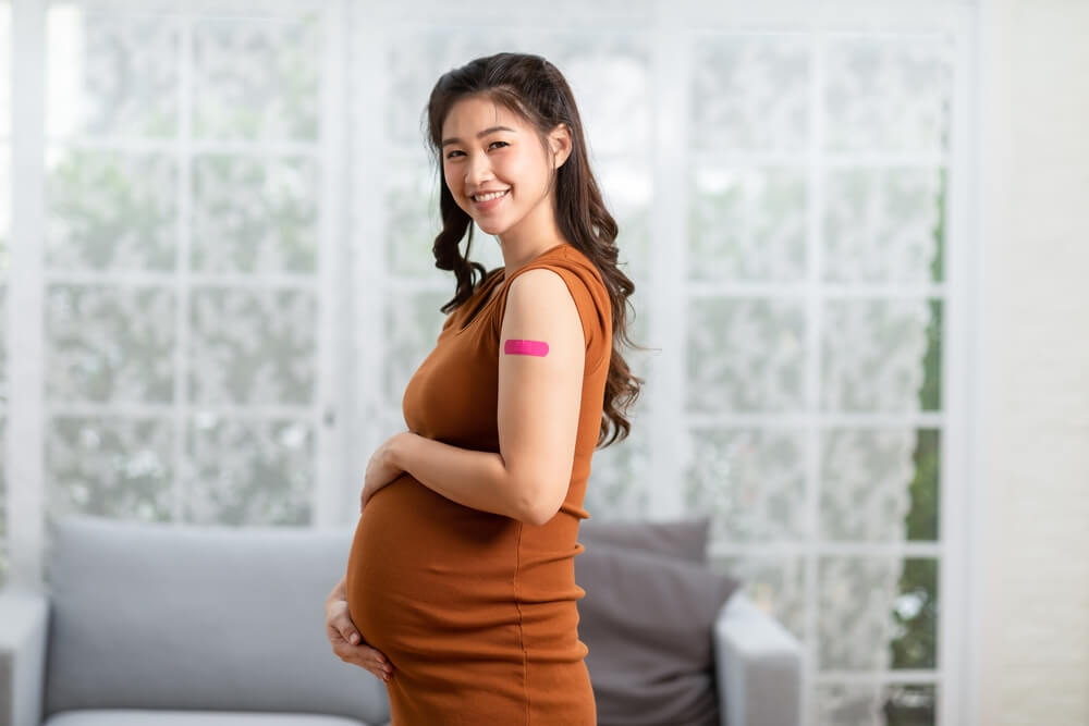 Happy pregnant woman received anti virus vaccine cheerful with bandage