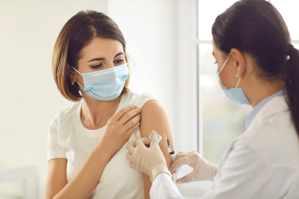 Young woman in medical face mask getting vaccine at doctor's office