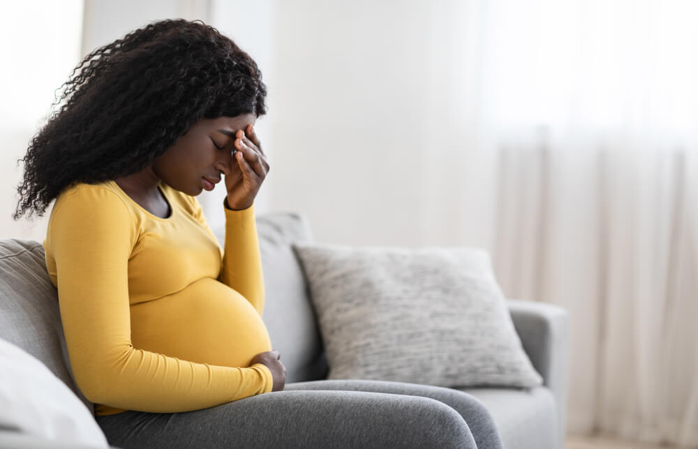 Young pregnant woman feeling sick, sitting on sofa at home