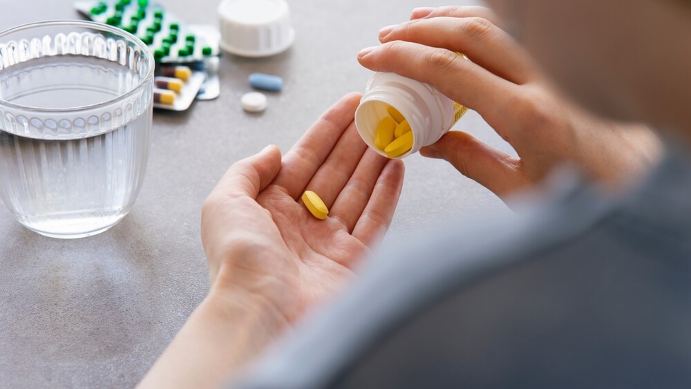 Close up woman holding pill in hand with water.