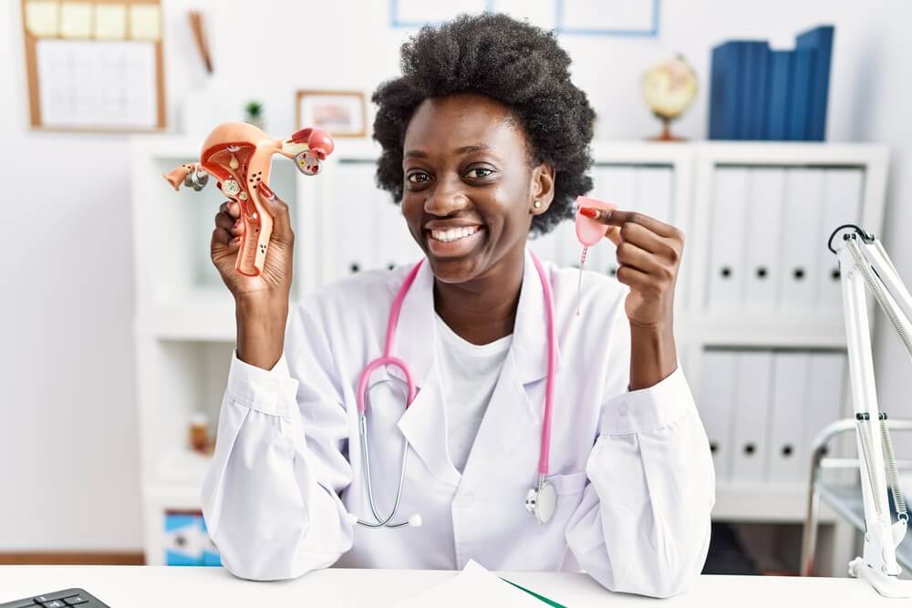 African Doctor Woman Holding Anatomical Female Genital Organ and Menstrual Cup Smiling With a Happy and Cool Smile on Face