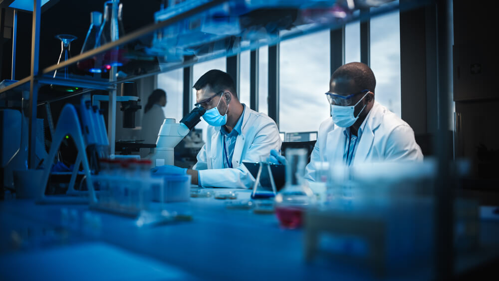 Two Scientists Wearing Face Masks Use Microscope