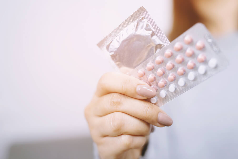 Woman Hand Holding Contraceptive Pills and Condom Sitting on Sofa Background.