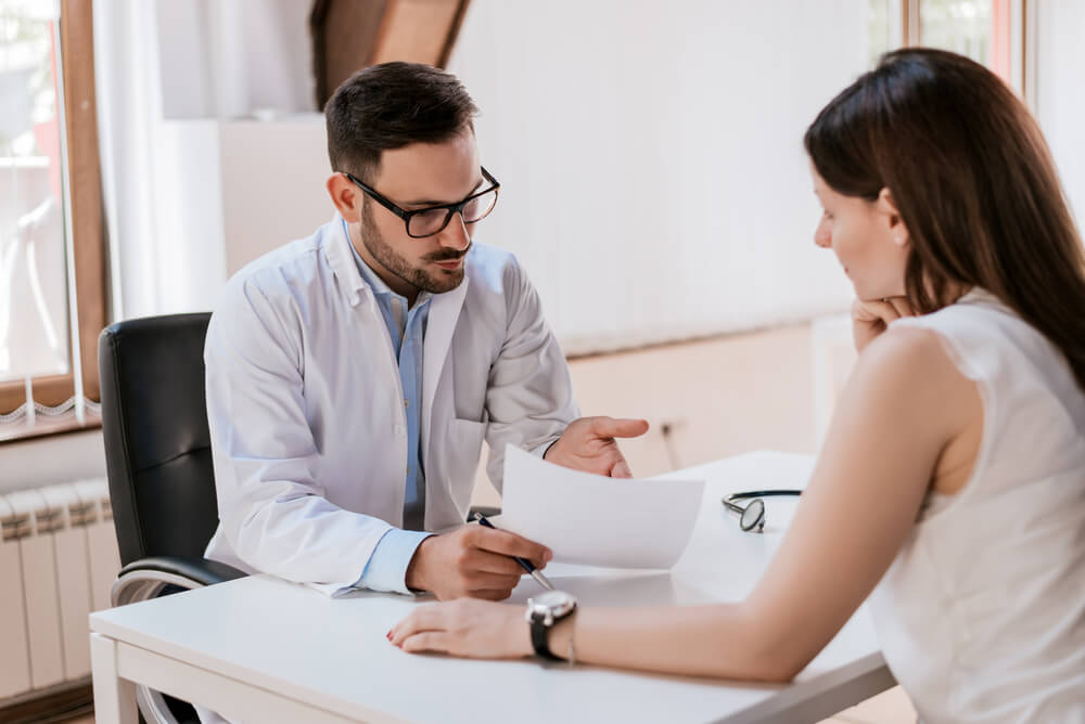 Male Doctor With Female Patient Reading Reports on Paper