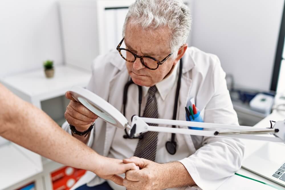Middle Age Grey-haired Man Wearing Dermatologist Uniform Examining Skin Arm Using Loupe at Dermatology Clinic