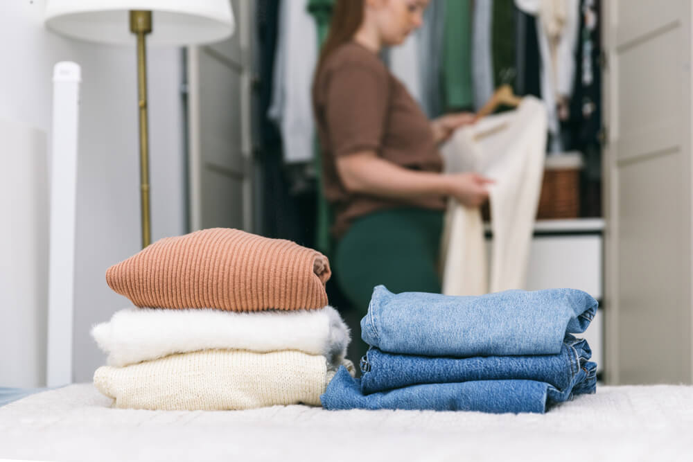 A Woman Is Cleaning Out Her Wardrobe, Standing by Clothes Placed on Hangers and in Drawers