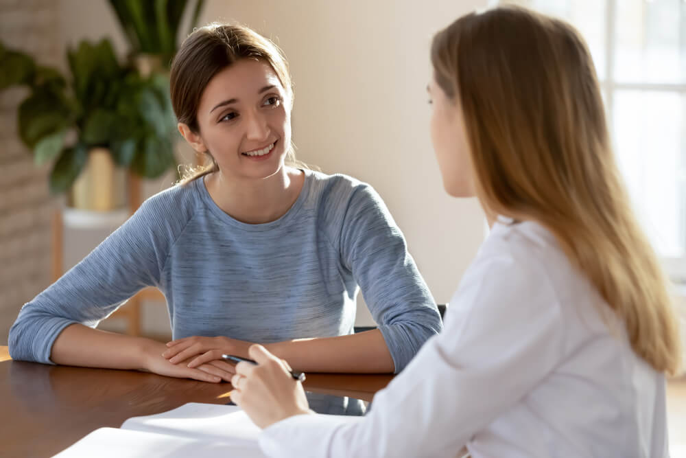 Smiling Young Woman Listening to Doctor Therapist at Meeting