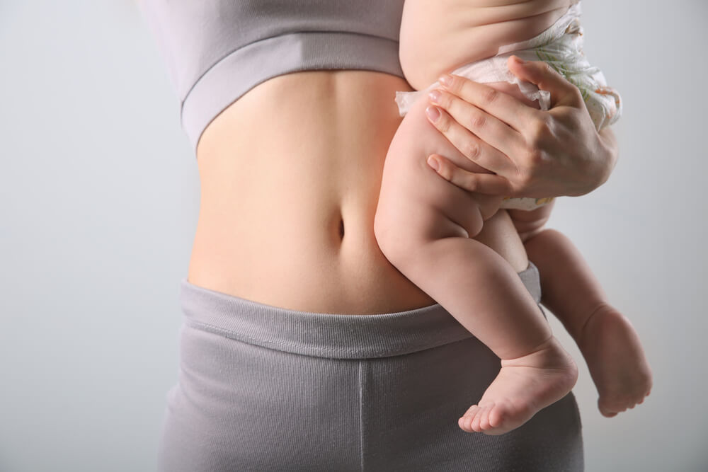 Mother With Bare Belly Holding Her Baby on Light Grey Background