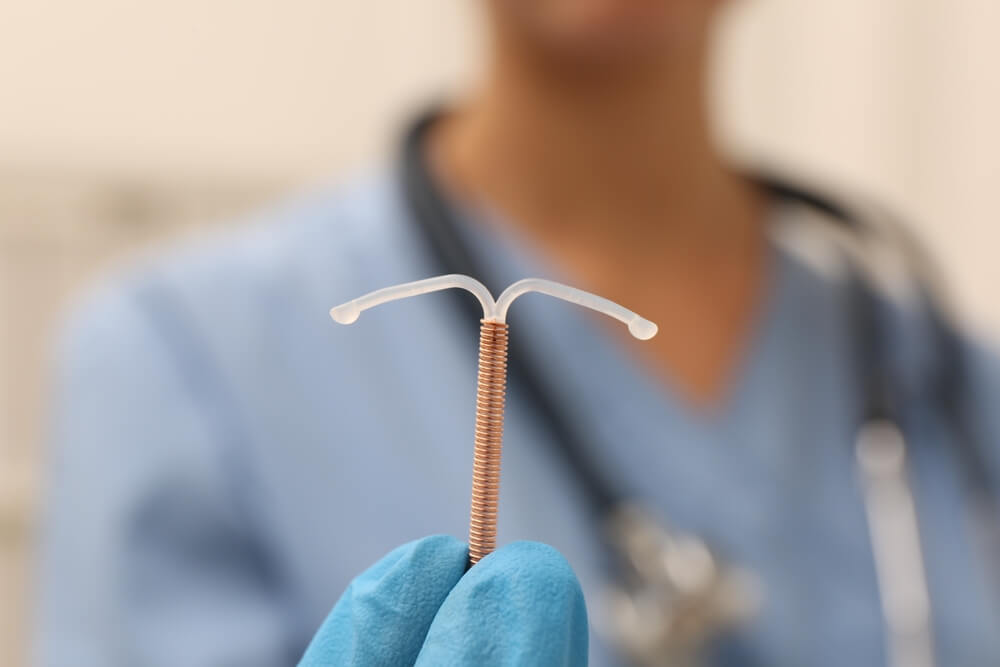 Doctor Holding T-Shaped Intrauterine Birth Control Device on Blurred Background, Closeup