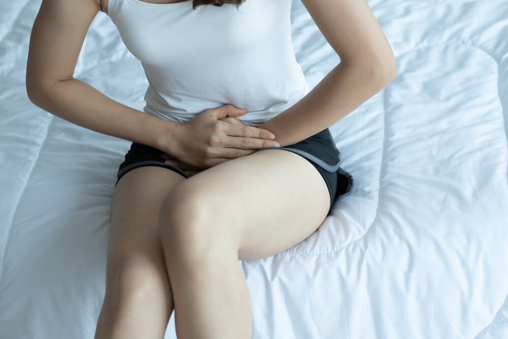 Woman Wearing White Shirt Sitting on Bed Have a Bladder Pain