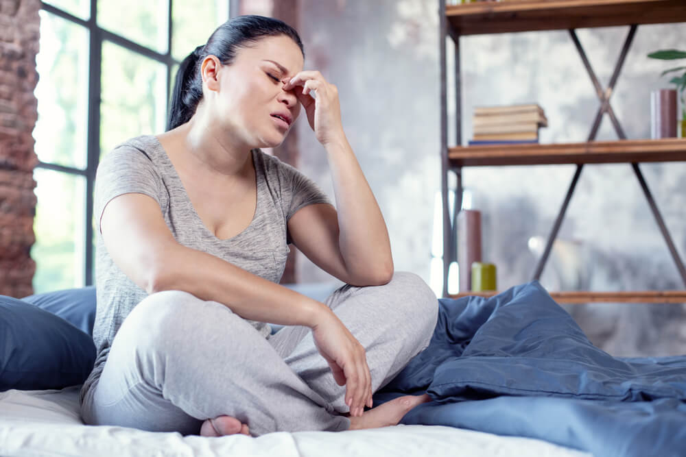 Low Angle of Sorrowful Emaciated Woman Staying on Bed and Massaging Nose Bridge