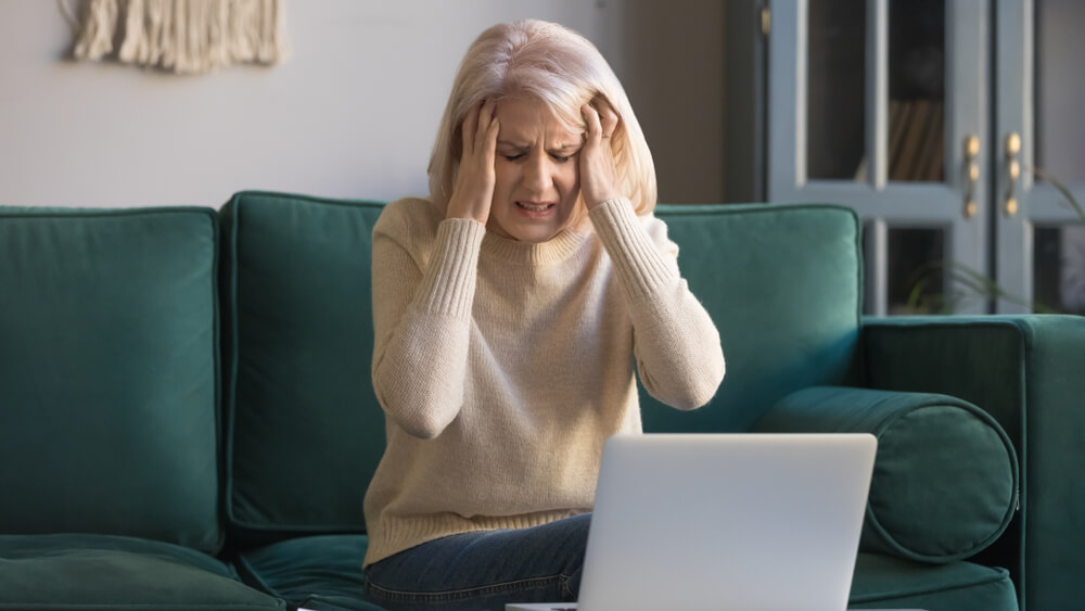 Mature Woman Sitting on Couch Near Laptop Touch Temples Suffers From Sharp Head Ache or Migraine After Long Usage of Computer