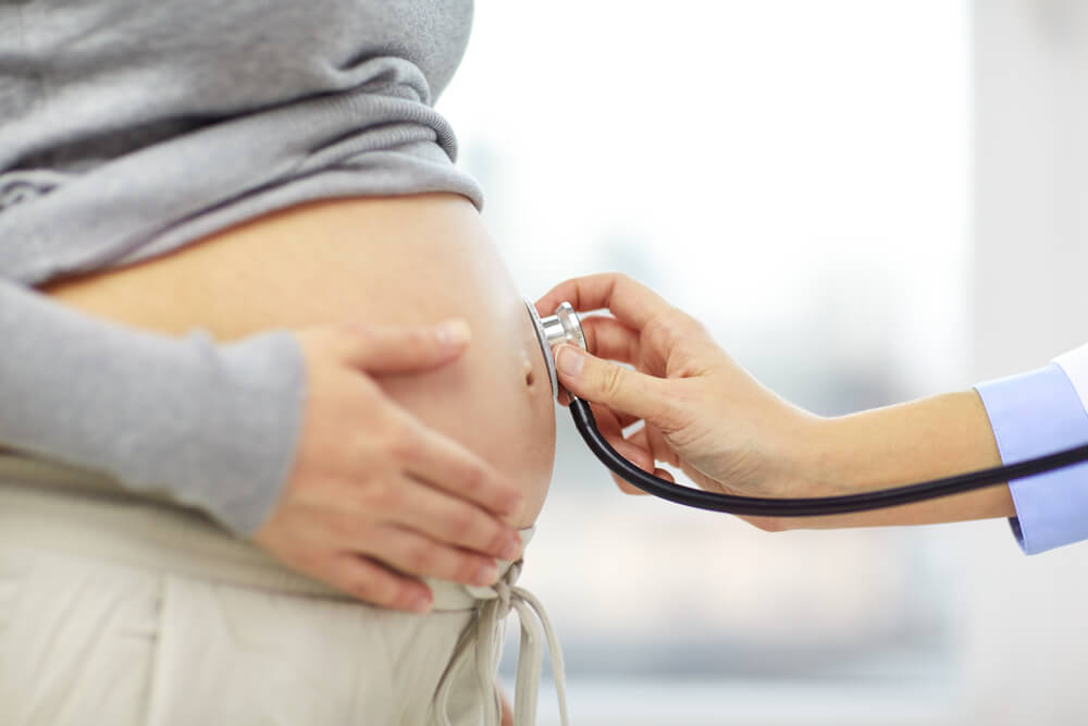 Pregnancy, Healthcare, People and Medicine Concept - Close Up of Pregnant Woman Belly and Doctor Hand With Stethoscope at Medical Appointment in Hospital