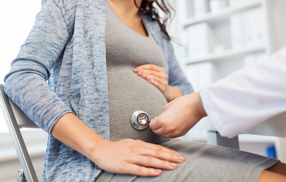 Gynecologist Doctor With Stethoscope Listening to Pregnant Woman Baby Heartbeat at Hospital