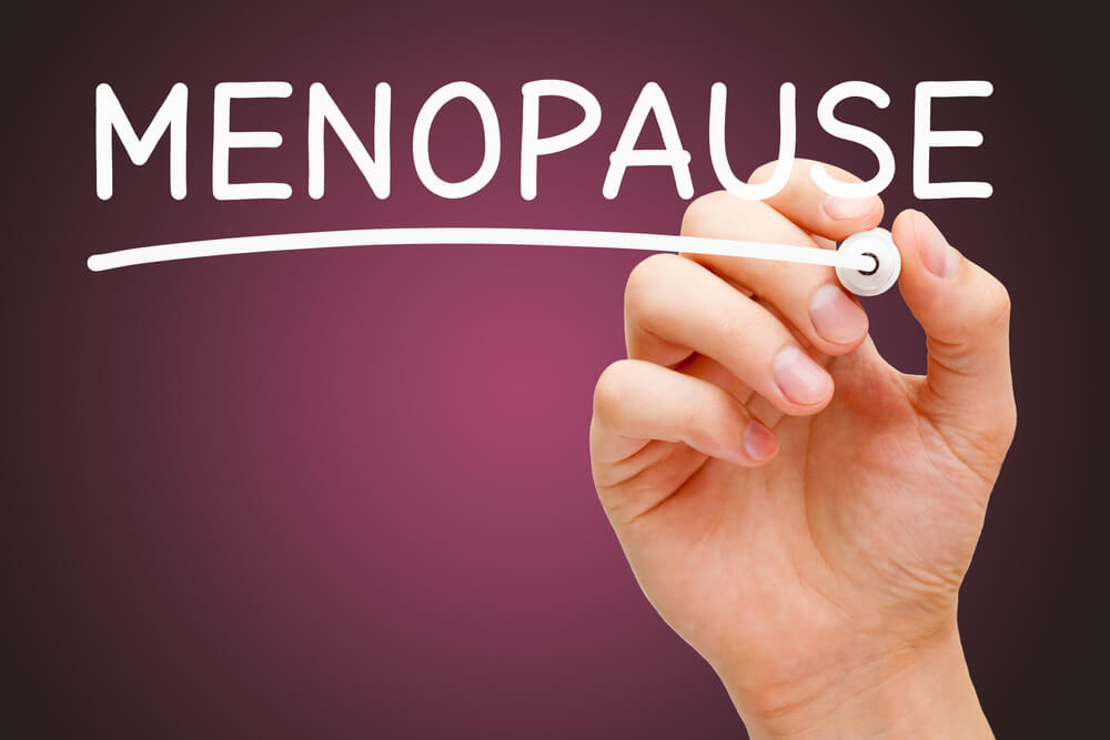 Hand Writing the Word Menopause With White Marker on Dark Pink Background