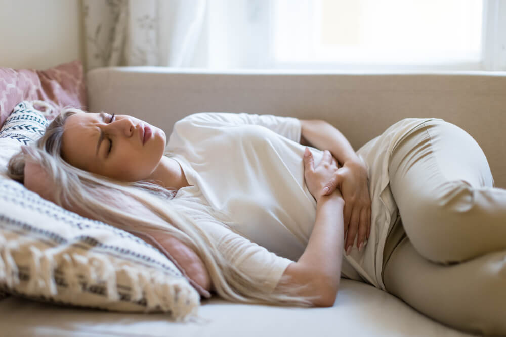 Young woman suffering from stomach pain, feeling abdominal pain or cramps, lying on sofa