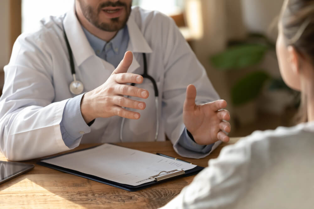 Young male doctor physician gesturing, explaining disease treatment results or examining female patient at checkup clinic