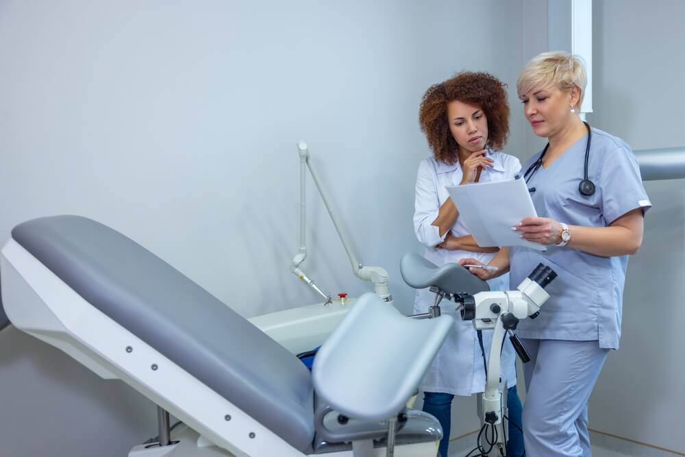 Two doctors standing near gynecological chair and discussing the diagnosis
