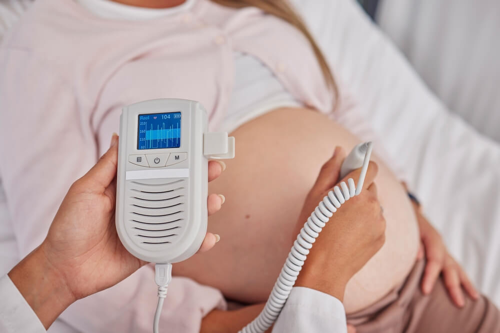 Pregnant woman and doctor hands with heart monitor for baby healthcare