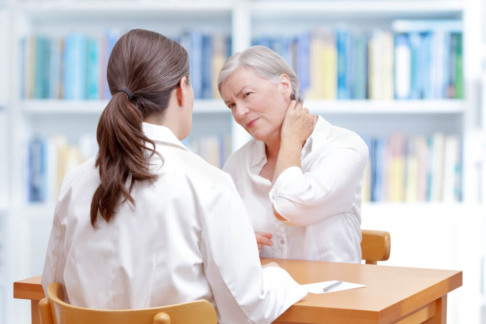 Senior female patient consulting her physician or doctor on account of chronic neck pain caused by osteoporosis
