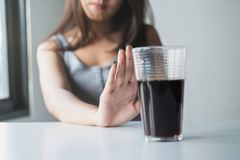 Young woman showing bad hand symbol to soft drink soda that have high sugar