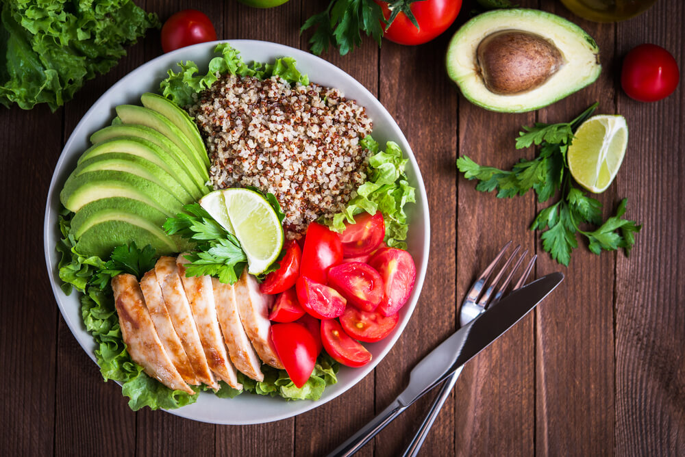 Healthy Salad Bowl With Quinoa, Tomatoes, Chicken, Avocado, Lime and Mixed Greens, Lettuce, Parsley on Wooden Background Top View.