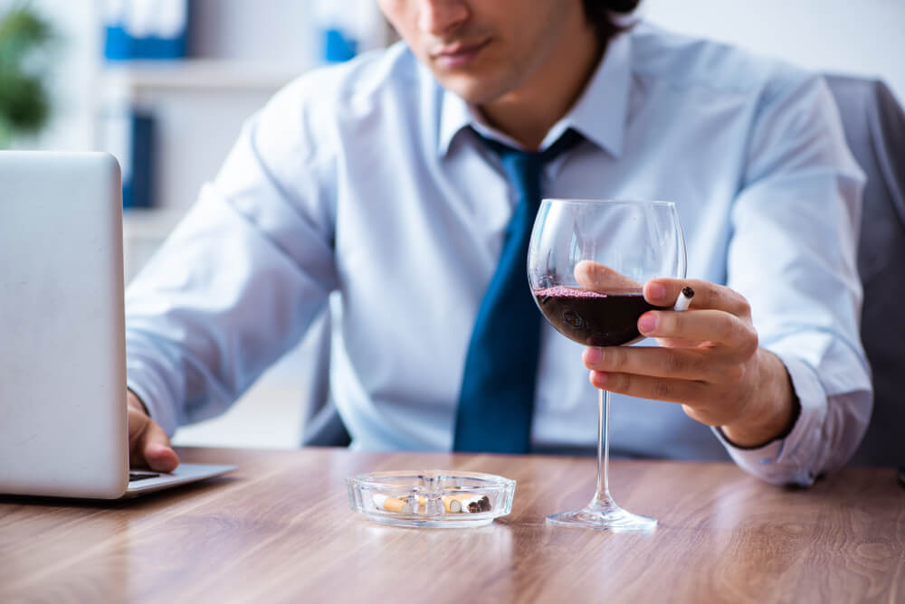 Male Employee Drinking Alcohol and Smoking Cigarettes at Workplace