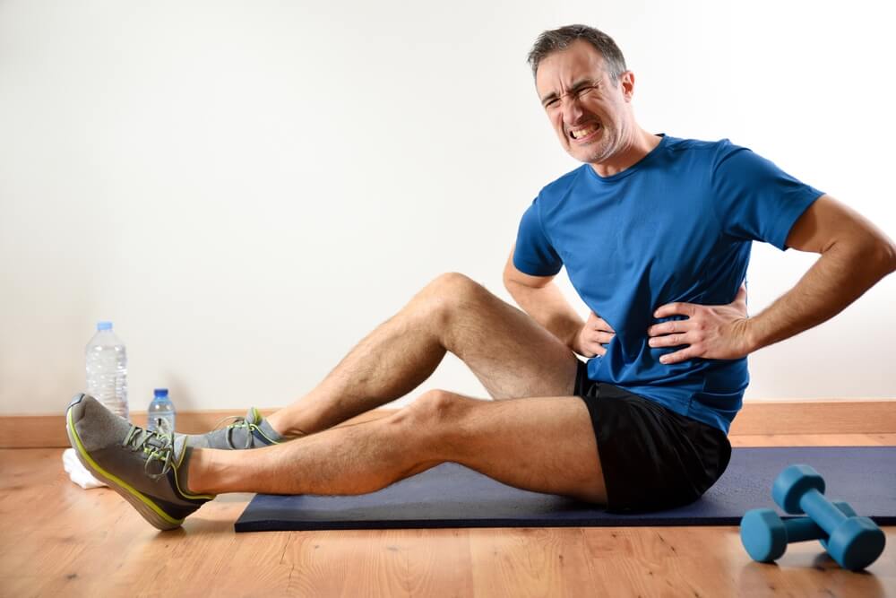 Man Doing Sports Indoors Complaining of Ribs Pain Sitting on a Mat Side View