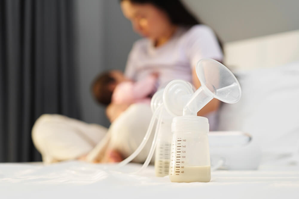 The Breast Milk Are In The Bottles Of Electric Breast Pumping Set On A Bed With Mother Breastfeeding Newborm Baby Background