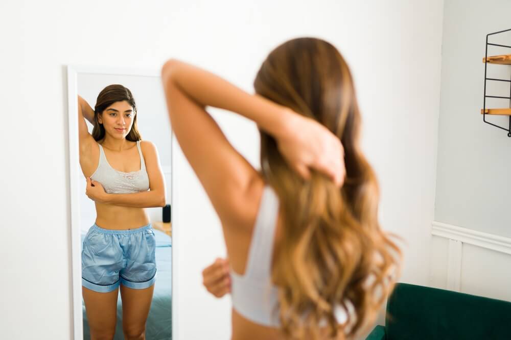 A young woman doing self exploration or exam in the mirror to prevent breast cancer.
