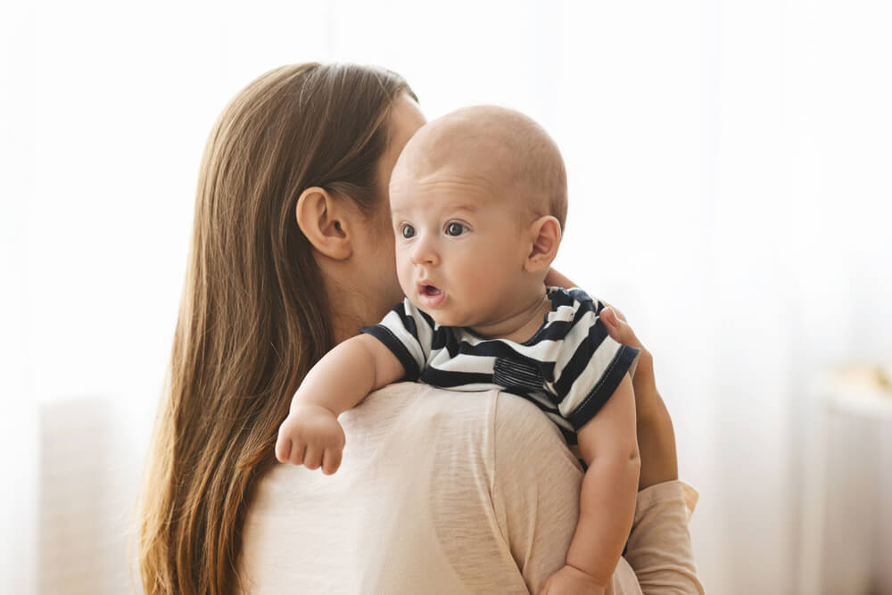 Burping Your Baby Concept. Woman Holding Newborn Baby on Hands and Patting His Back After Breasfeeding, Closeup