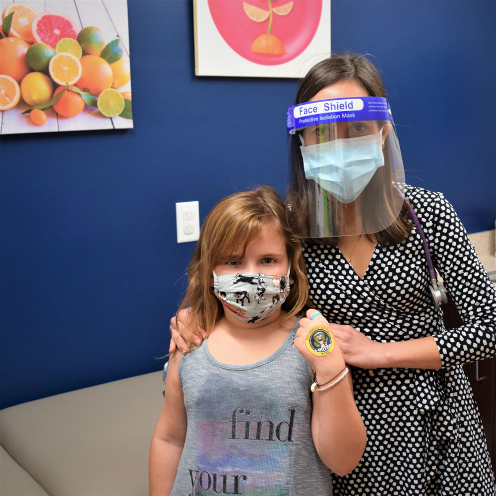 Mother With a Face Shield Holding Her Daughter With a Face Mask by Her Shoulders