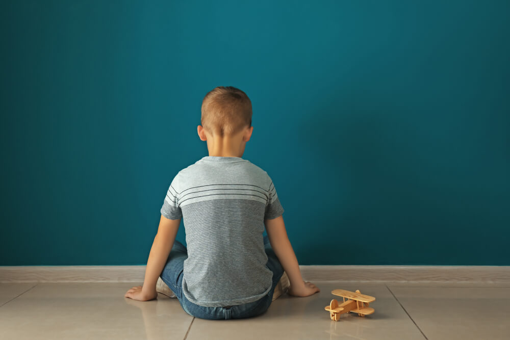 Little Boy Sitting Near Dark Wall in Empty Room