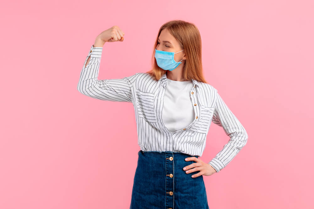 Happy Healthy Strong Young Woman in a Medical Protective Mask on Her Face, Showing Biceps on Her Arm