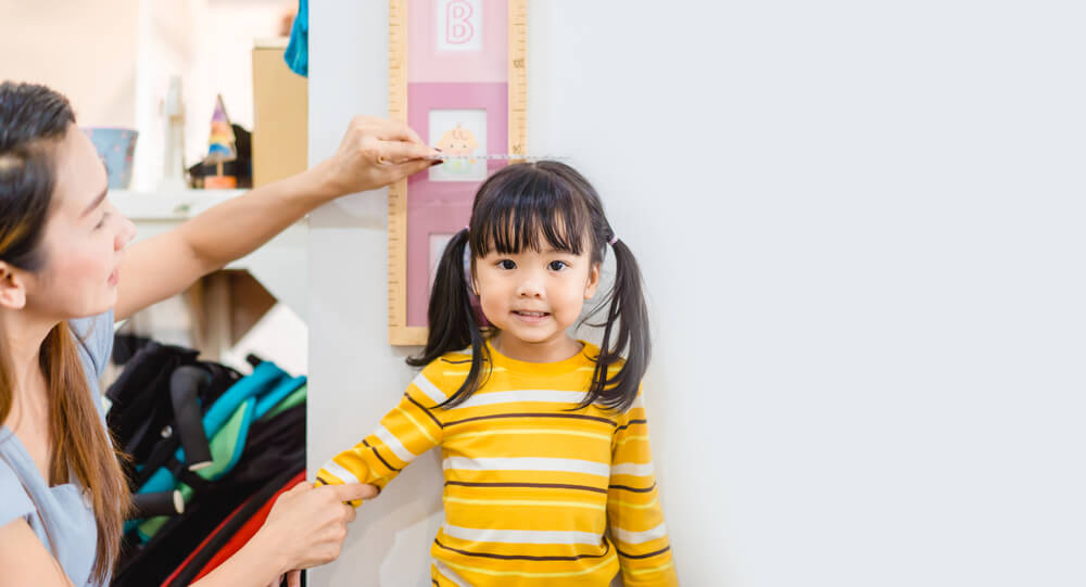 Mother Measuring Her Daughter's Height Near White Wall at Home