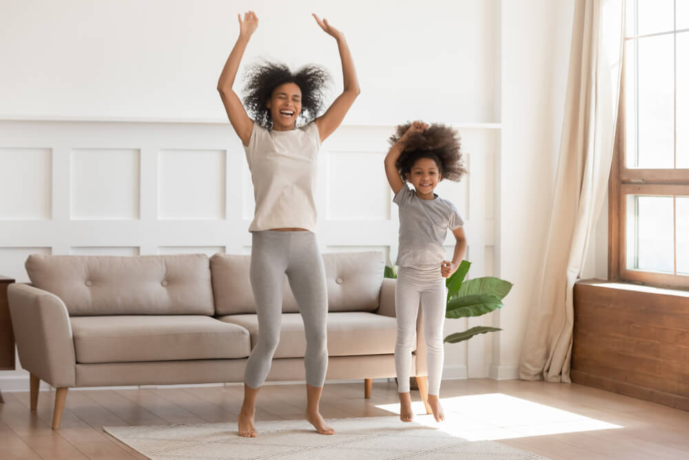 Carefree Funny African Family Young Mom Having Fun With Cute Little Kid Girl Jump Dancing in Living Room