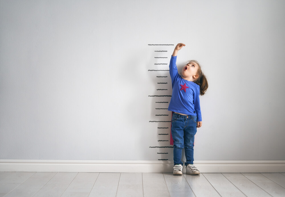 Kid Is Measuring the Growth on the Background of Wall.