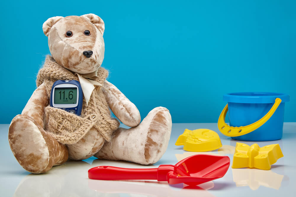 Teddy Bear With a Glucometer and Scattered Children’s Toys on a Blue Background. The Concept of Treatment of Diabetes in Children, Hyperglycemia, Pediatric Doctor