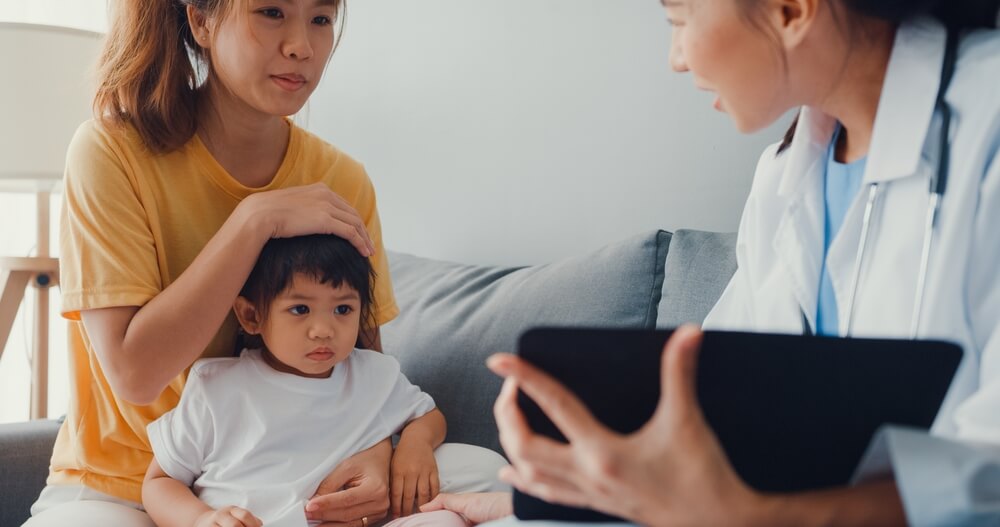 Doctor and Little Girl Patient Using Digital Tablet Sharing Good Health Test News With Happy Mom Sit On Couch in House