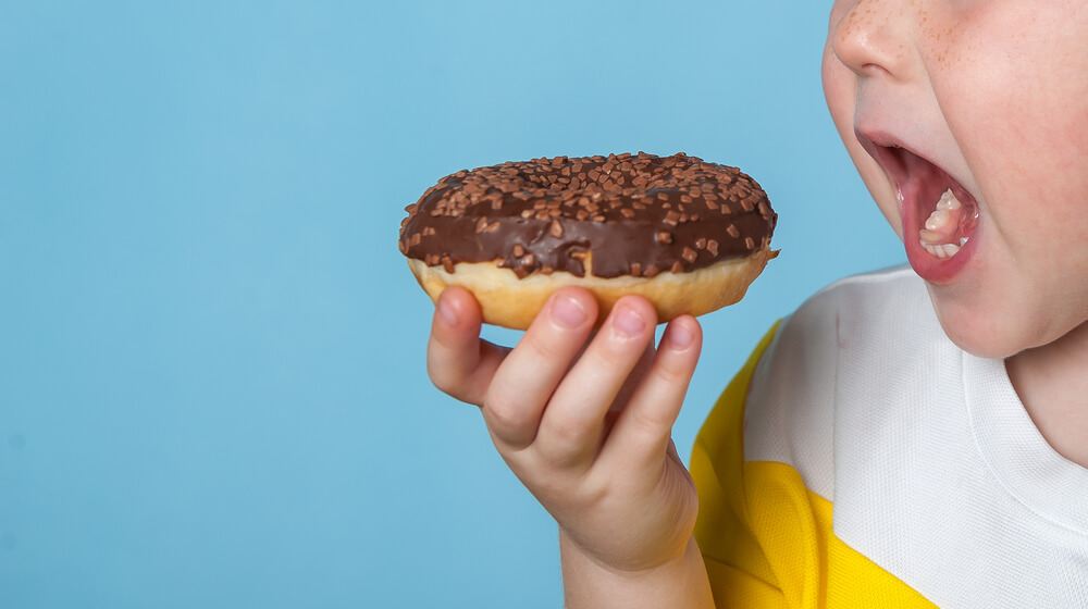 Little Happy Cute Boy Is Eating Donut on Blue Background Wall.