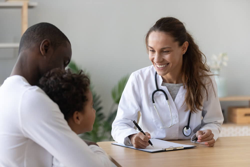 Smiling Female Doctor Listen Consult Cute Boy Make Notes in Patient Card at Medical Checkup Appointment