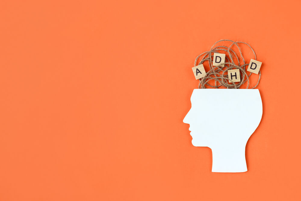 Silhouette Of Human Head And Wooden Blocks With The Letters ADHD On Orange Background
