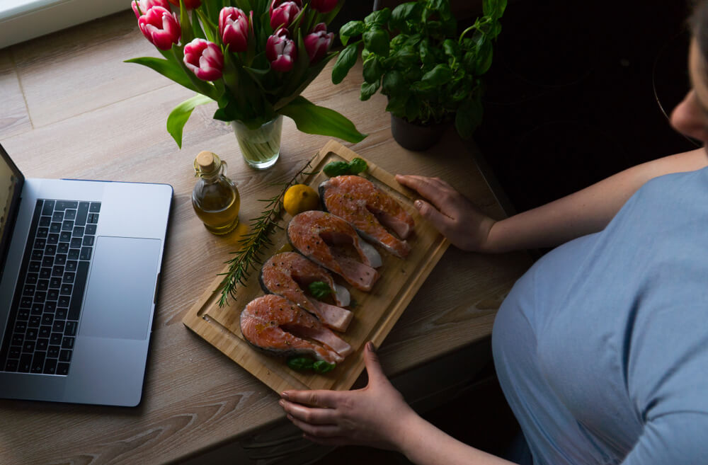 Pregnant Girl Is Watching Online Course and Preparing Salmon With Rosemary and Lemon for Lunch.