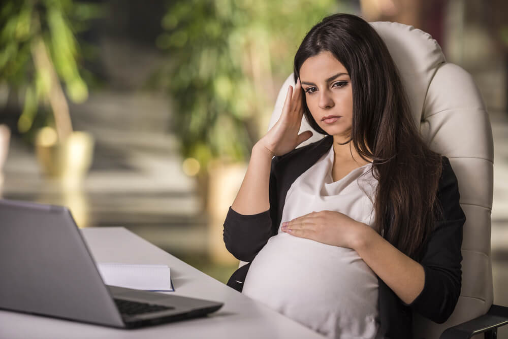 Pregnant Adult Businesswoman Working With Laptop Looking Stressed in Office.