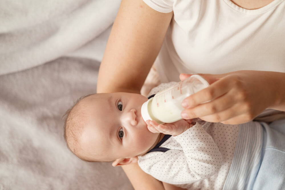 Baby Drinks Milk From a Bottle and Looks at Camera