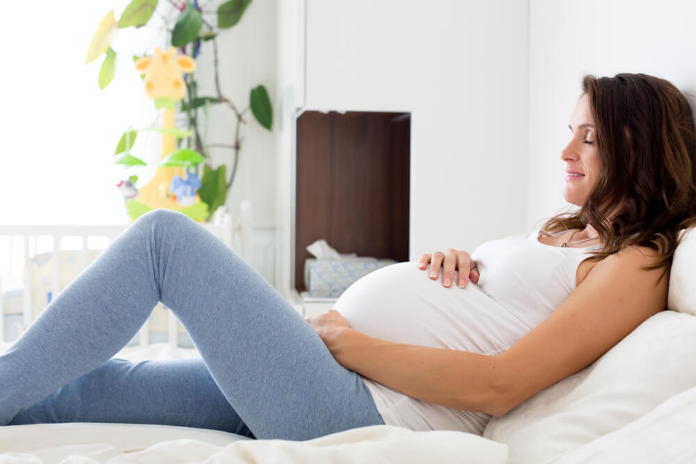 Happy Young Beautiful Pregnant Woman, Sitting on Bed in Bedroom, Preparing to Give a Birth