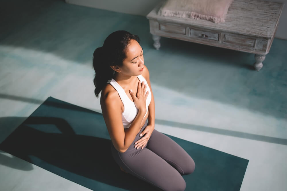 Asian Girl Practicing Yoga in Diaphragmatic Breath Pose at Spacious Home.